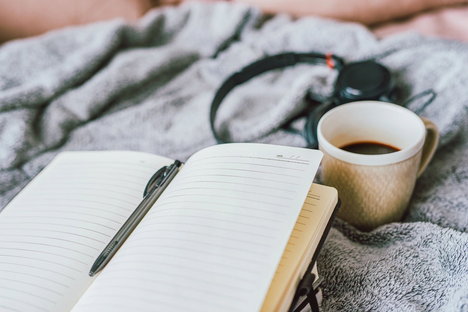 Notebook, coffee and headphones on a bed at home